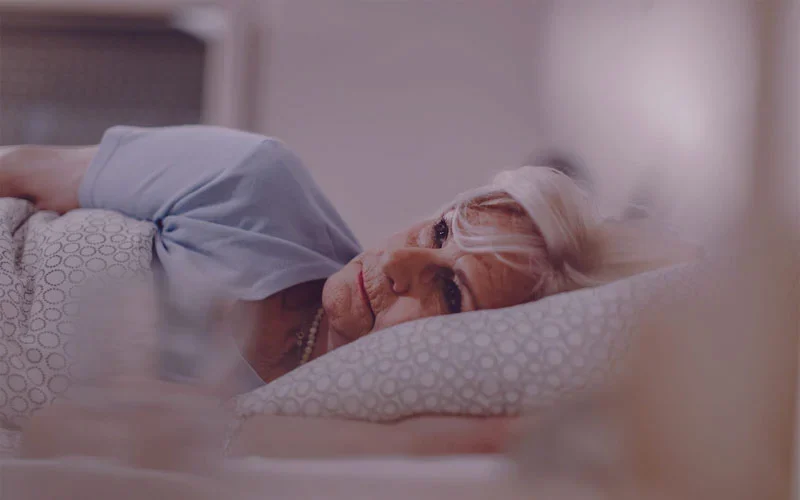 خانم مسنی که بر روی تخت دراز کشیده است و با بی‌خوابی دست و پنجه نرم می‌کند